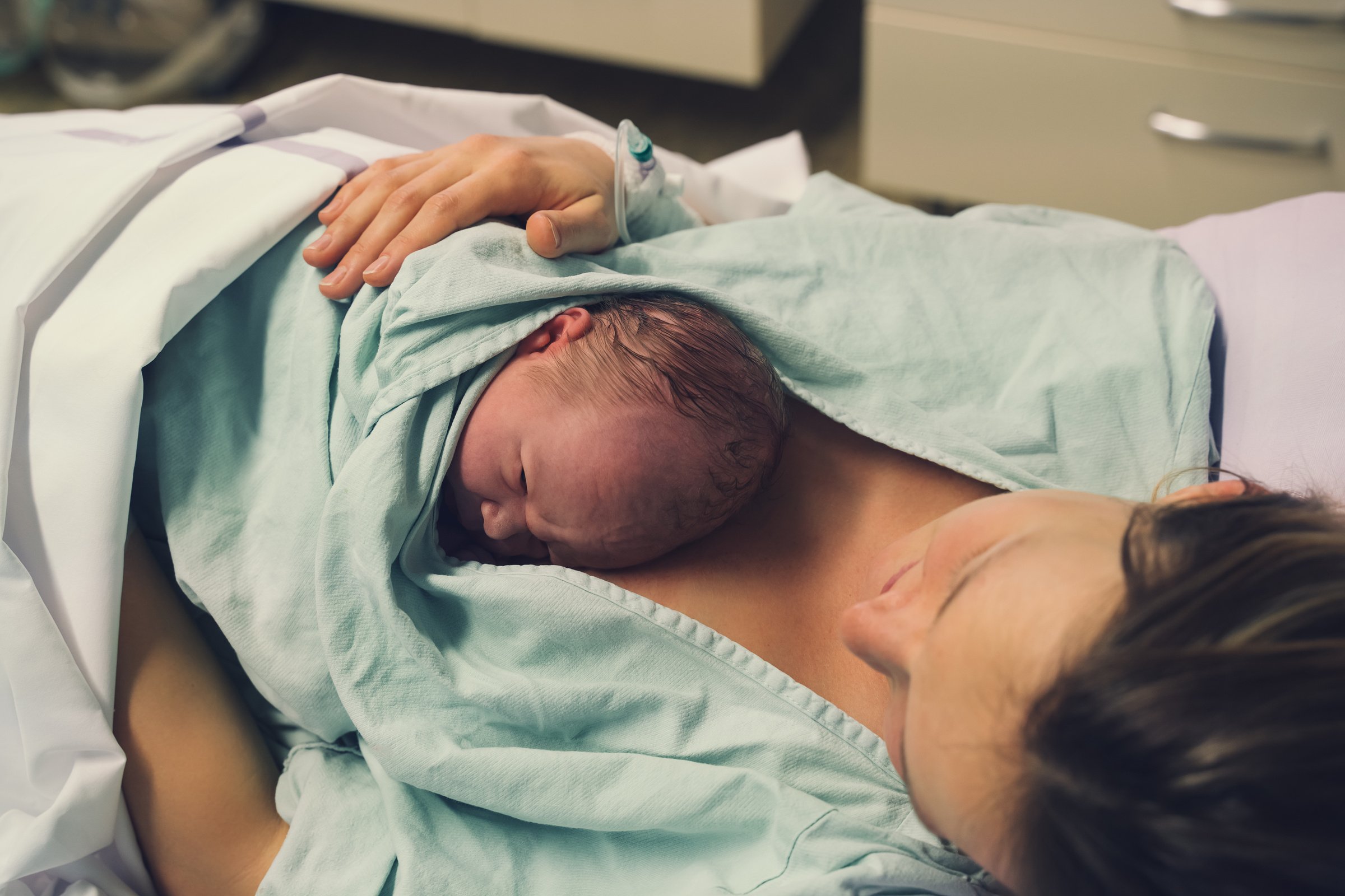 Mother and newborn. Child birth in maternity hospital. Young mom hugging her newborn baby after delivery. Woman giving birth.